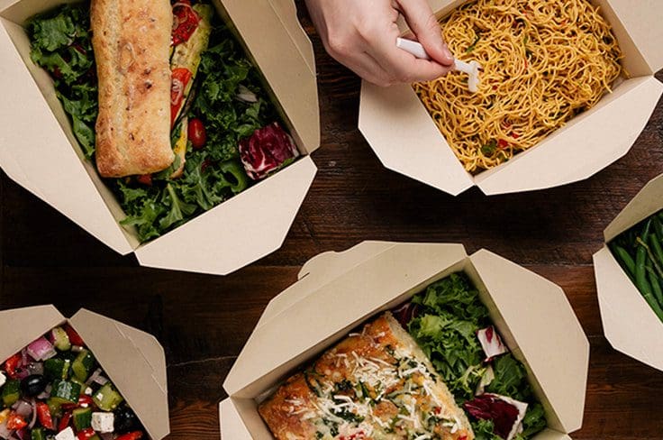 A top angle view of a couple takeout boxes with food and a hand with a fork in the takeout box with noodles.